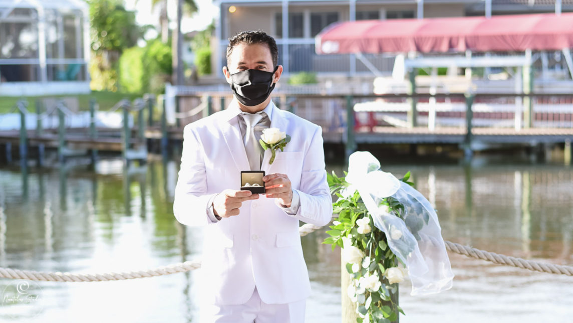 Photo showing groom with facemask holding wedding bands in Florida