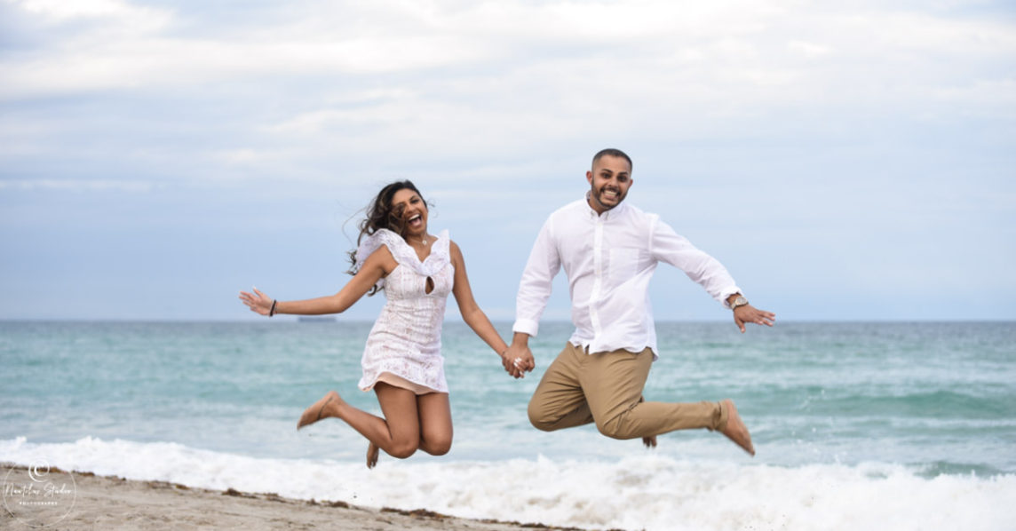 Photo of couple jumping after marriage proposal on the beach