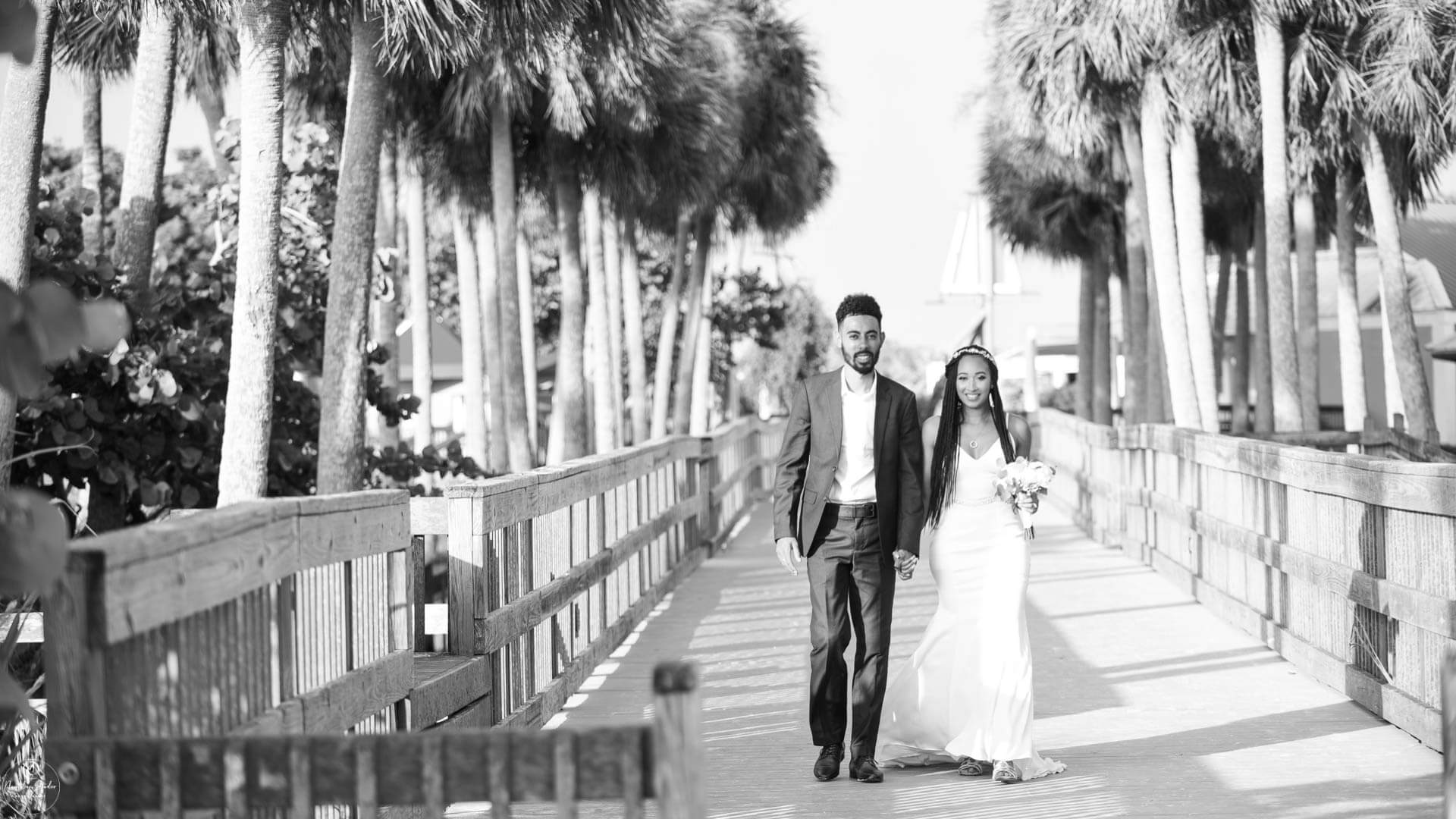 Lifestyle wedding photo of couple walking on boardwalk with palm trees
