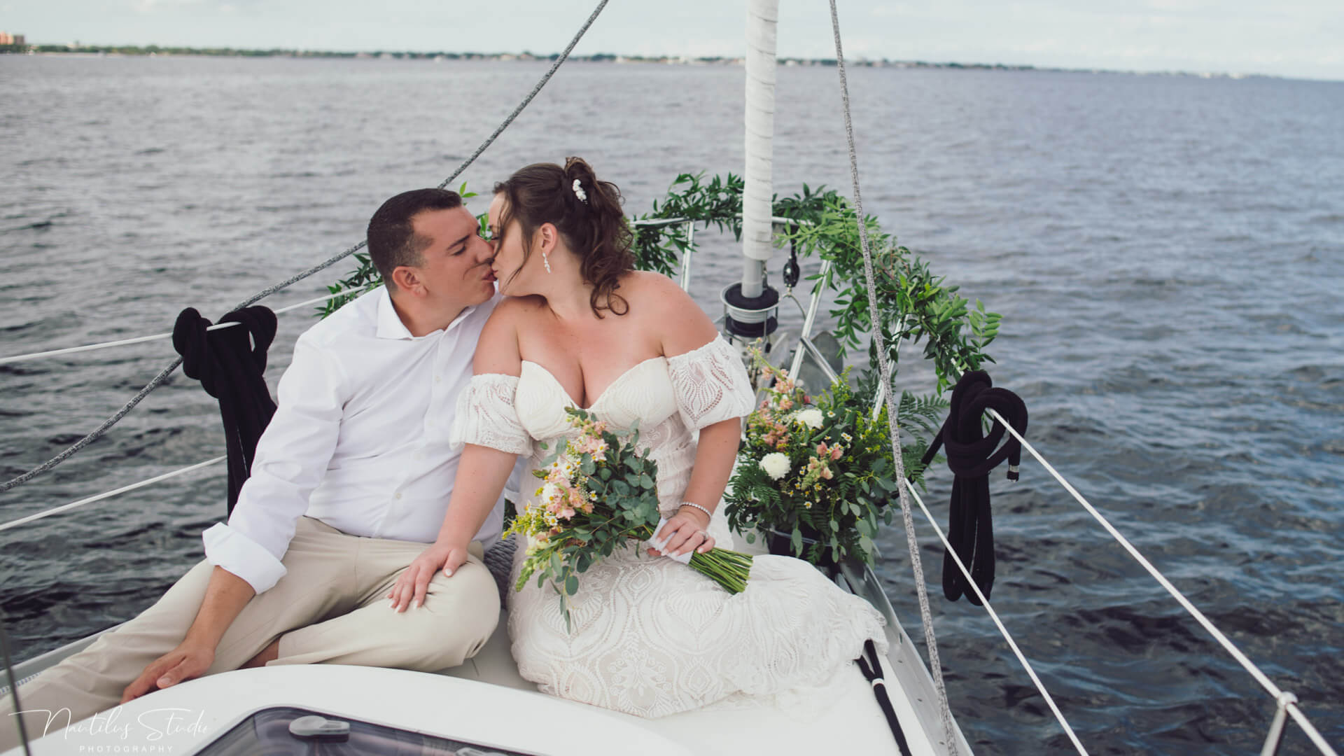 Photo wedding couple kissing at the bow of their sailboat