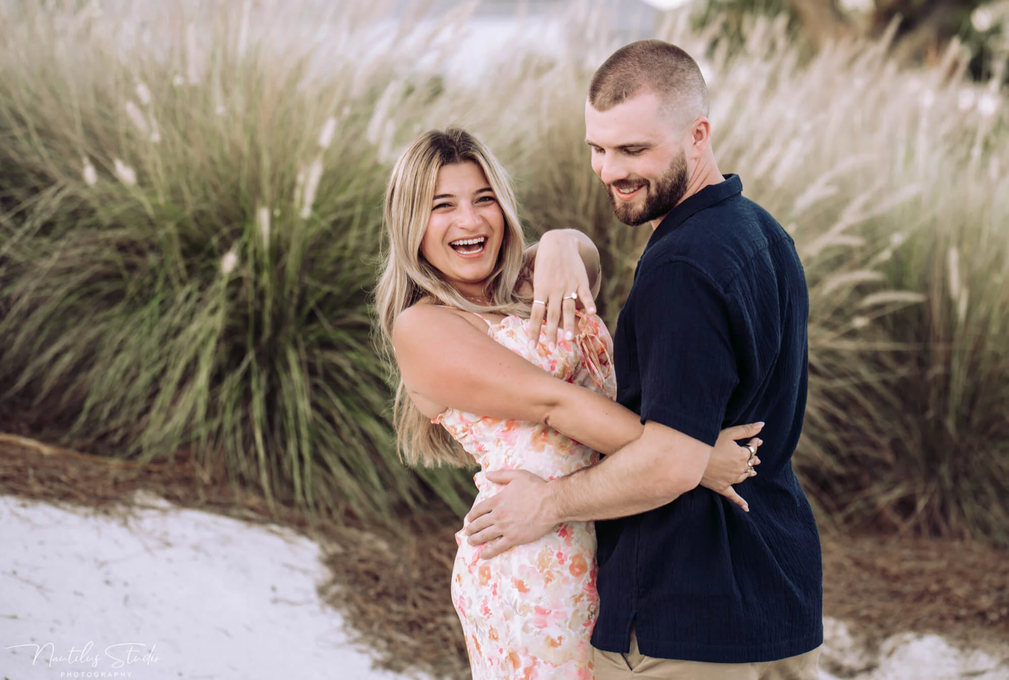 Photo of newly engaged couple laughing while she is showing her engagement ring.